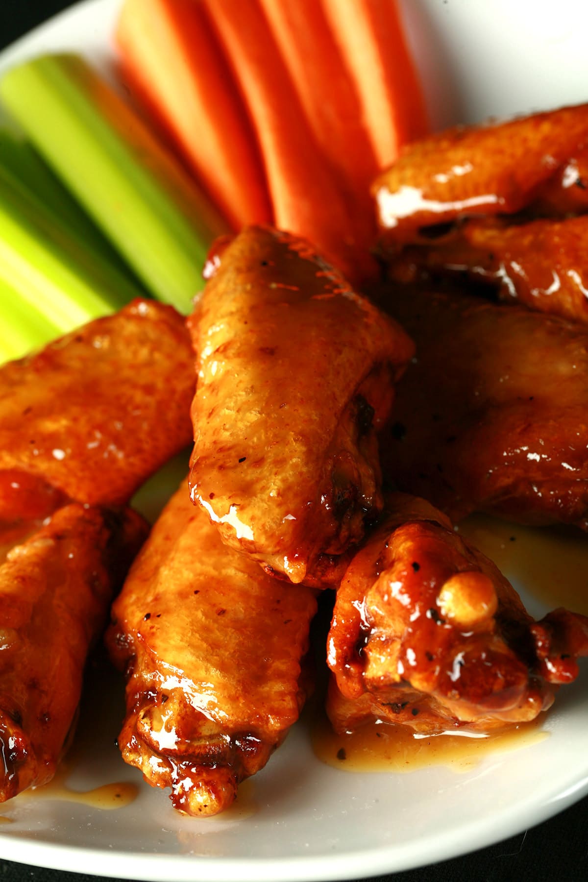 A small white plate with a pile of Whisky Honey Mustard Glazed Wings piled on it, celery and carrot sticks on the side.