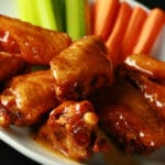 A small white plate with a pile of Whisky Honey Mustard Wings piled on it, celery and carrot sticks on the side.