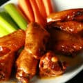 A small white plate with a pile of Whisky Honey Mustard Wings piled on it, celery and carrot sticks on the side.