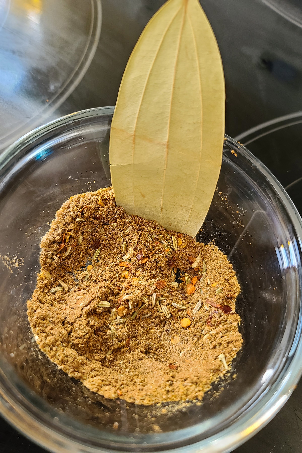 A small bowl of spices with a bay leaf sticking out of it.