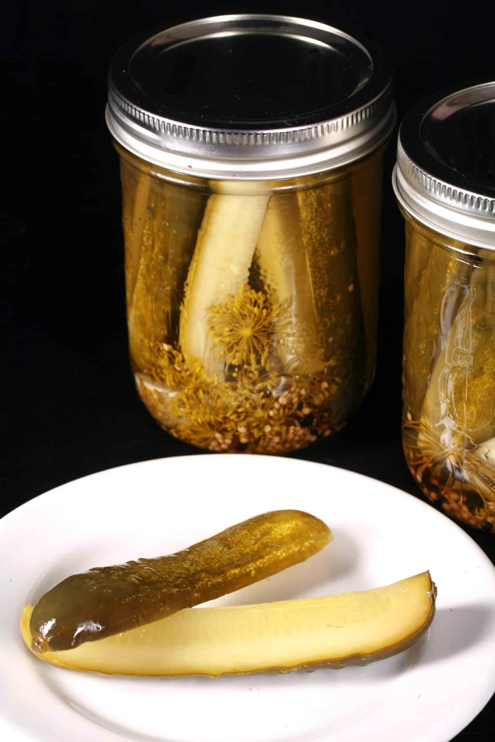 A pickle spears in front of several jars of homemade dill pickles.