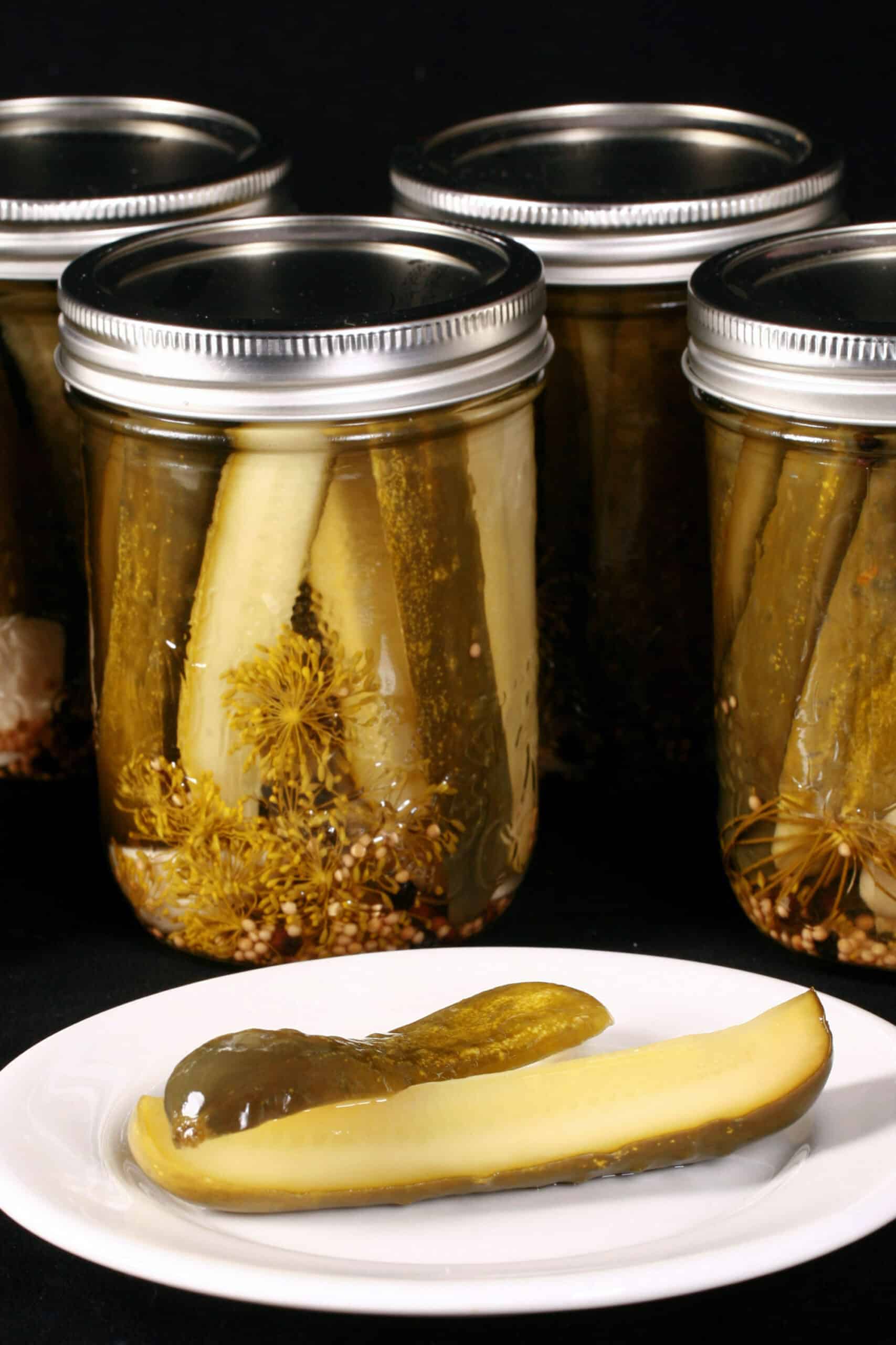A pickle spears in front of several jars of homemade dill pickles.