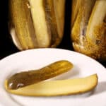 A pickle spears in front of several jars of homemade dill pickles.