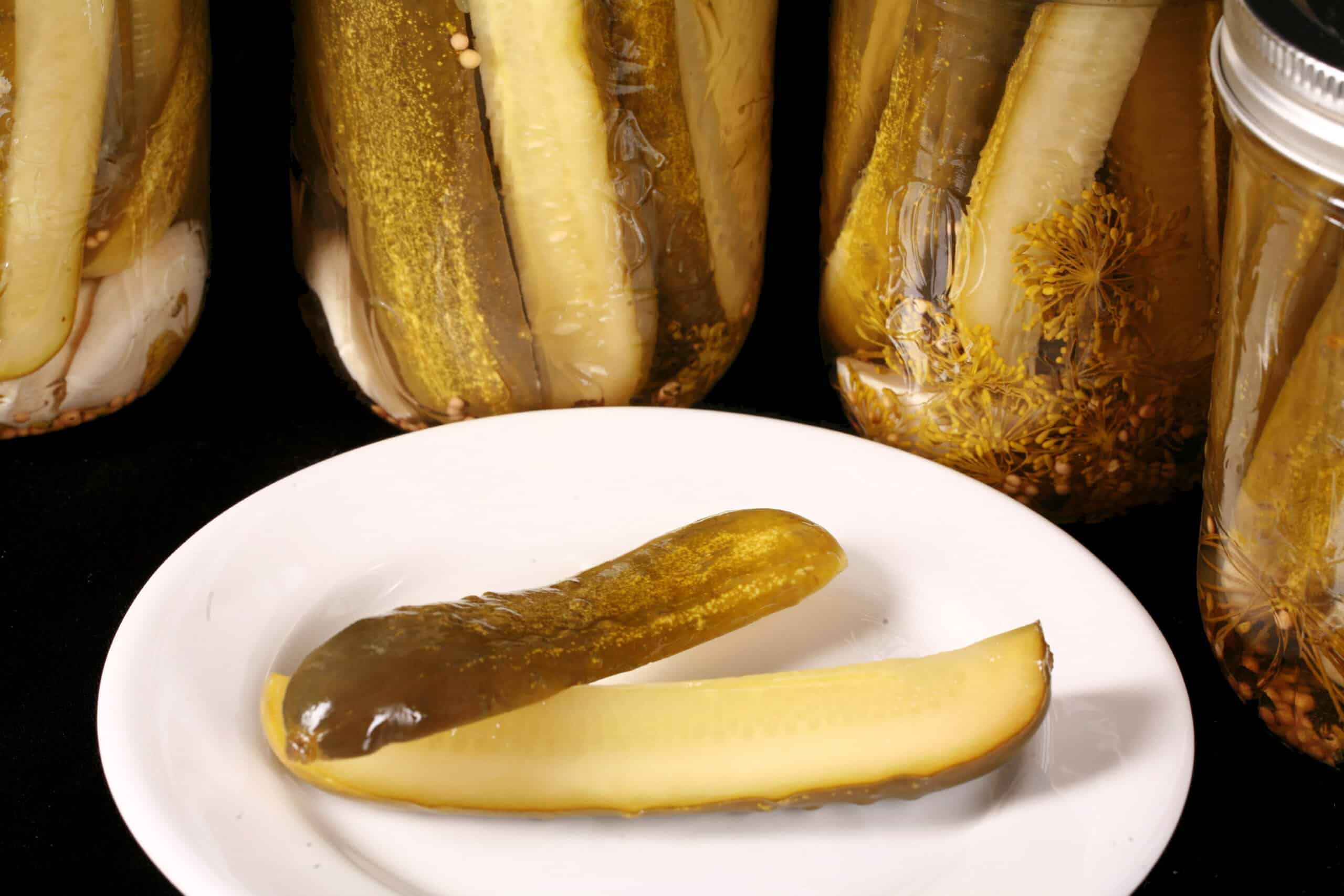 A pickle spears in front of several jars of homemade dill pickles.