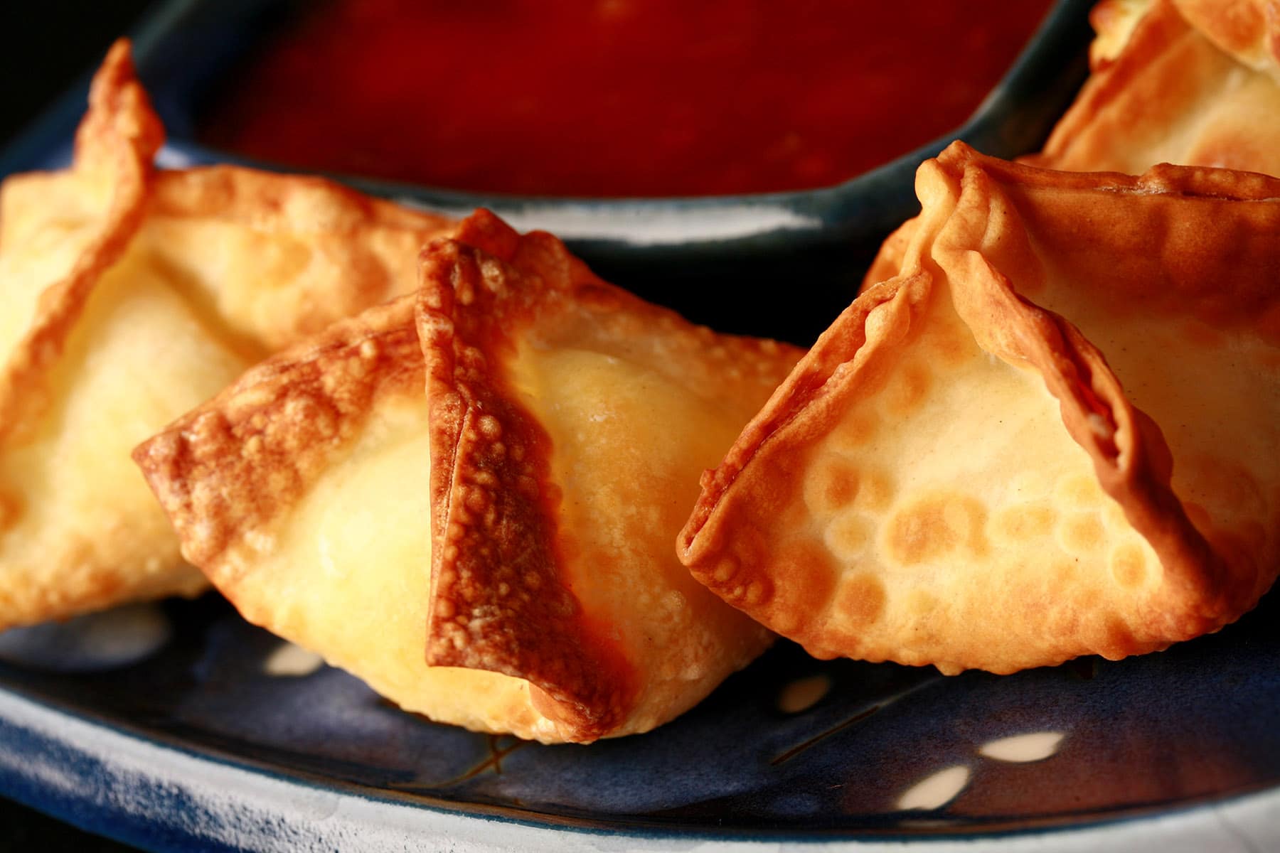 A small, blue, rectangular dish with pyramid shaped air fryer cream cheese wontons on it.