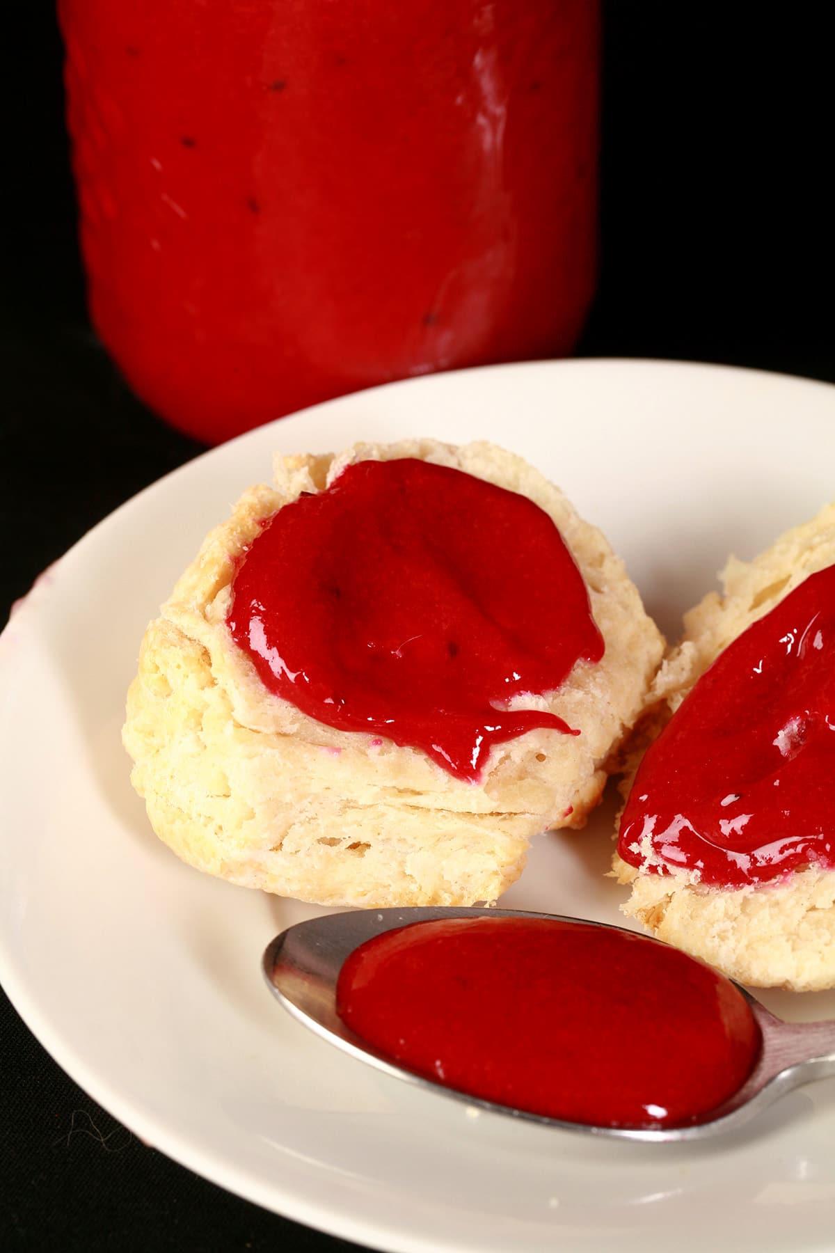 2 biscuits topped with blackcurrant curd, along with a spoon of the curd on the same plate.