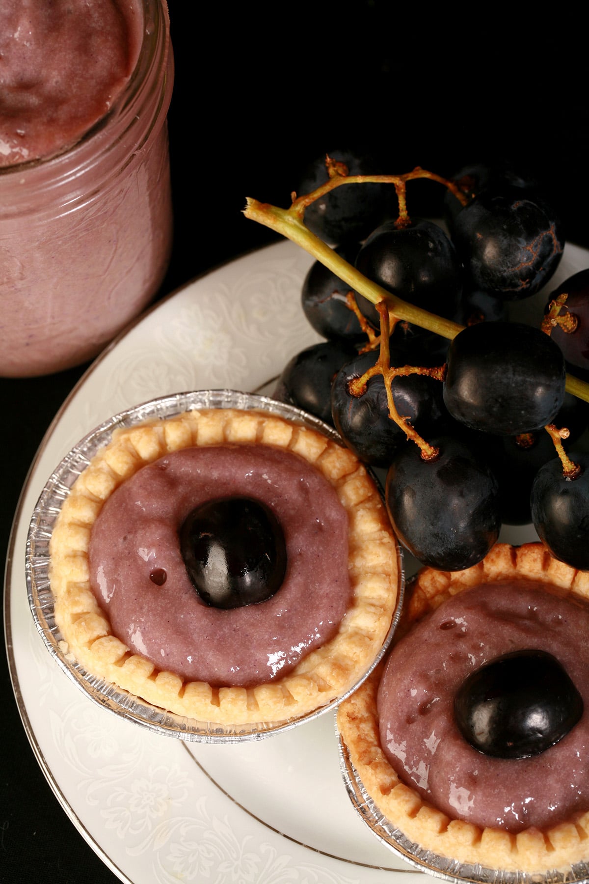 Two grape tarts on a plate, along with some fresh grapes.