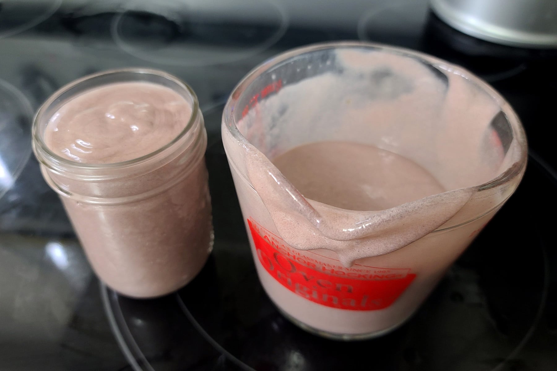 A jar of grape curd next to a glass measuring cup of fresh curd.