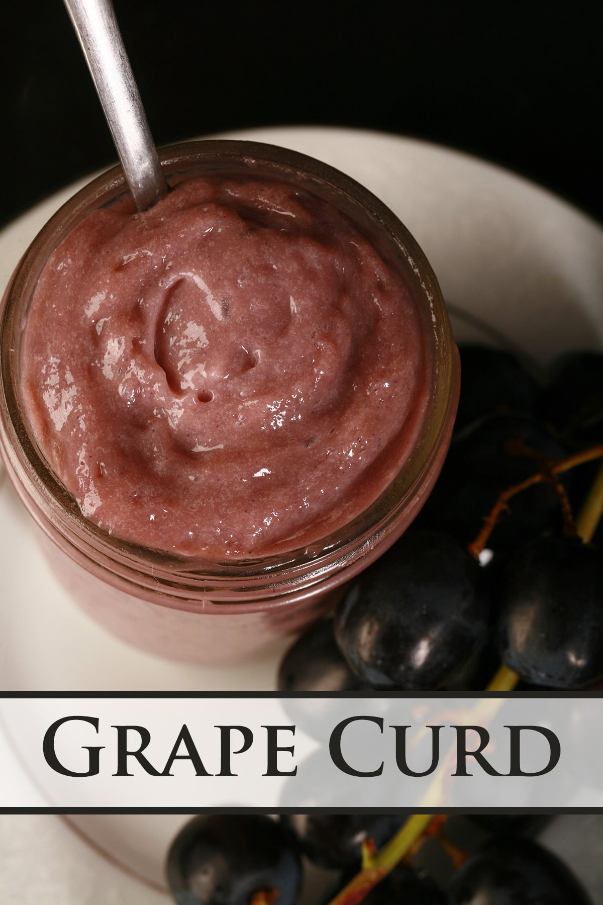 A jar of grape curd on a plate, along with some fresh grapes.