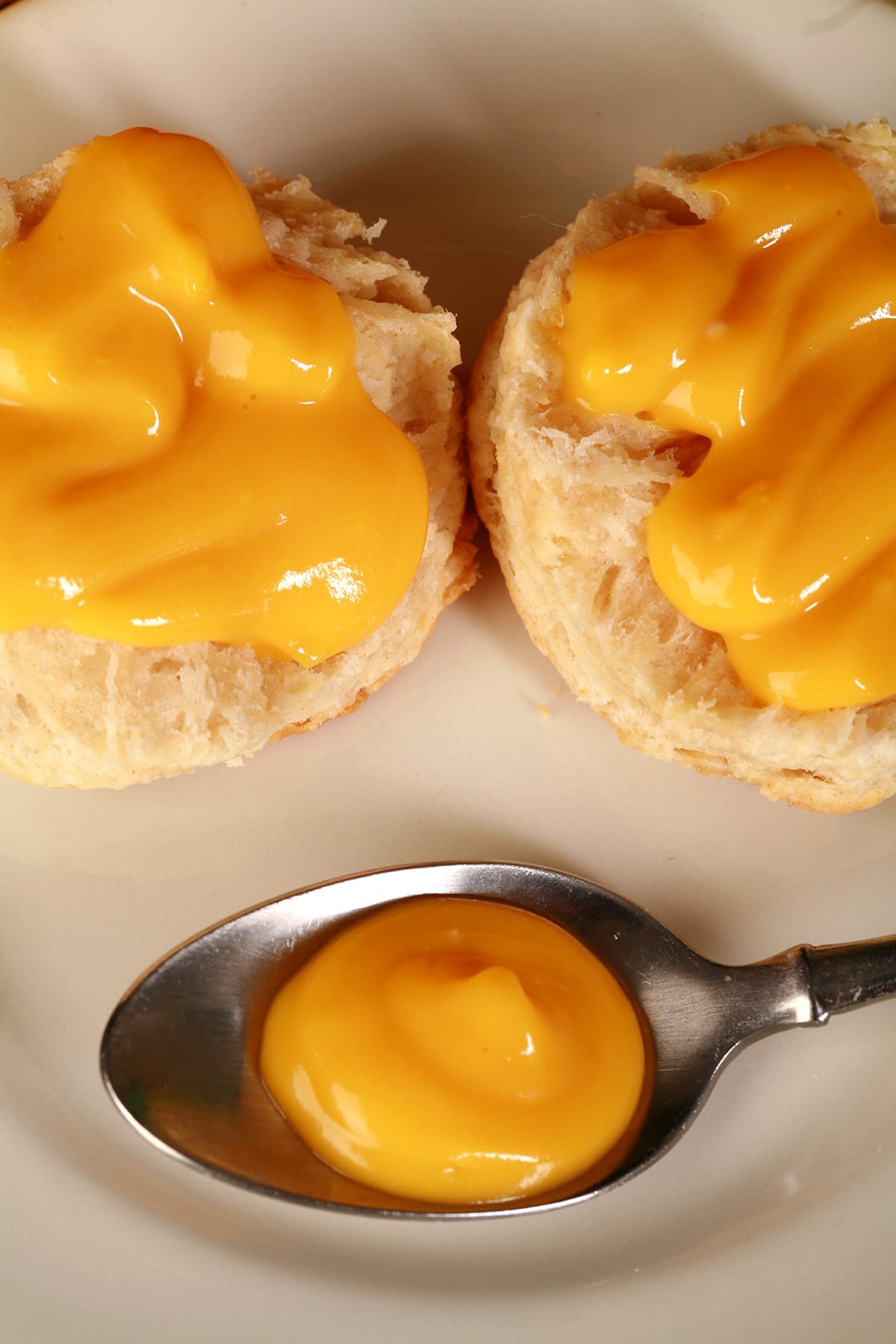 Two biscuits topped with mango curd, and a spoon of curd on a plate.