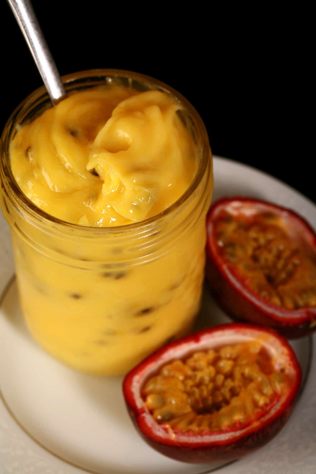 A jar of passionfruit curd on a plate, along with a sliced passionfruit.