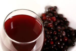 A glass of blackcurrant wine, with a small dish of black currants next to it.