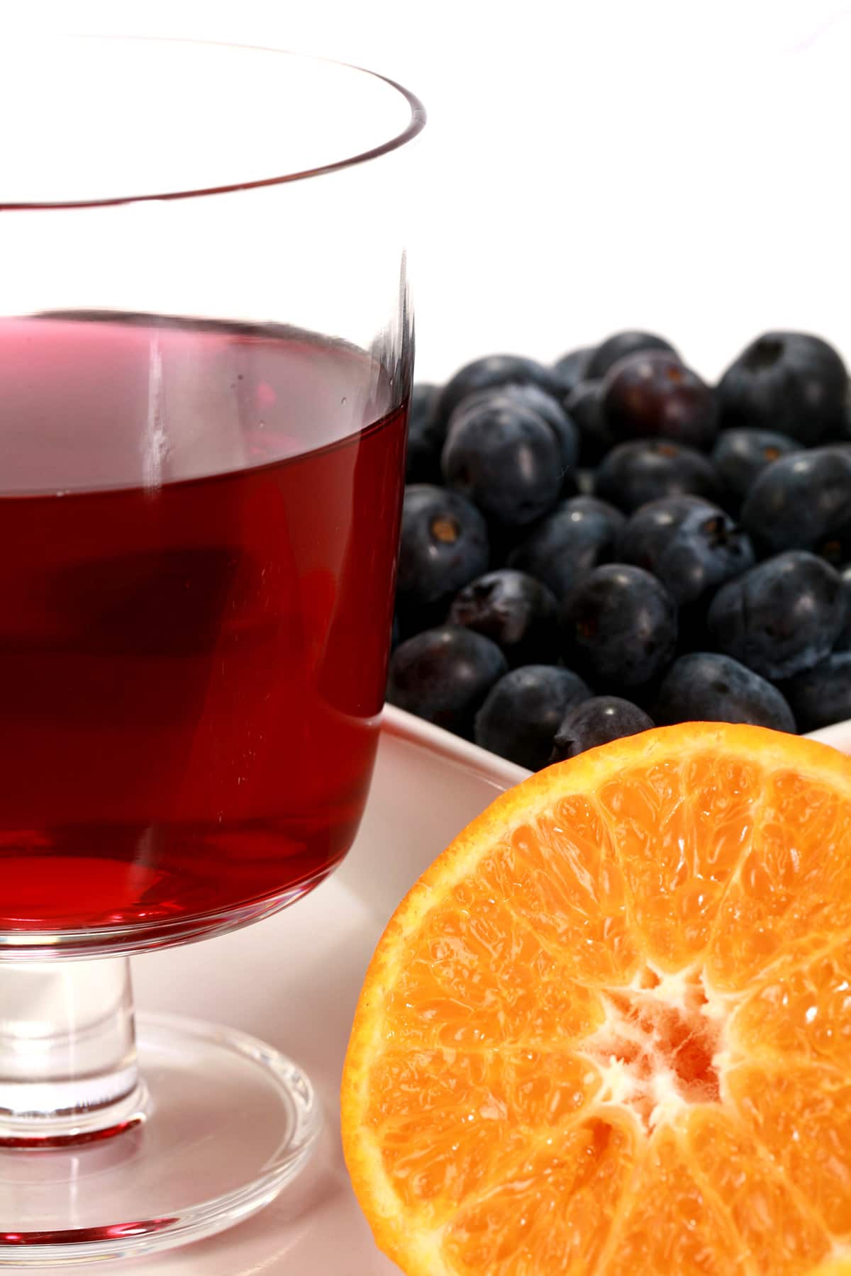 A wine glass of a medium purple blueberry clementine mead, with a dish of blueberries and a halved clementine next to it.