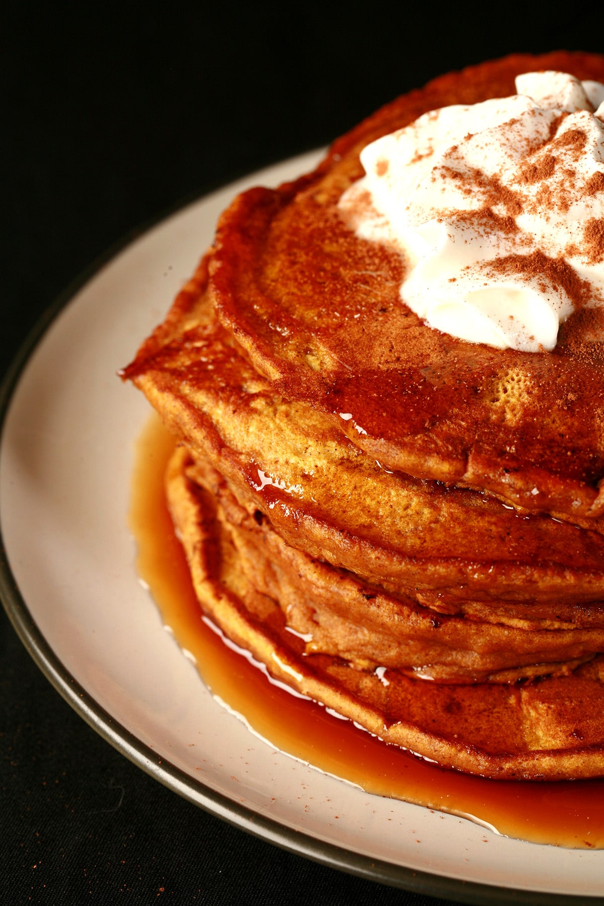 A tall stack of easy pumpkin pancakes, topped with whipped cream.