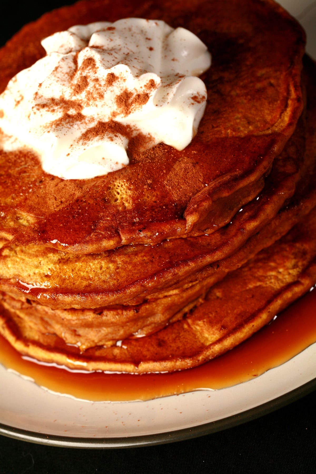 A tall stack of fluffy pumpkin pancakes, topped with whipped cream.