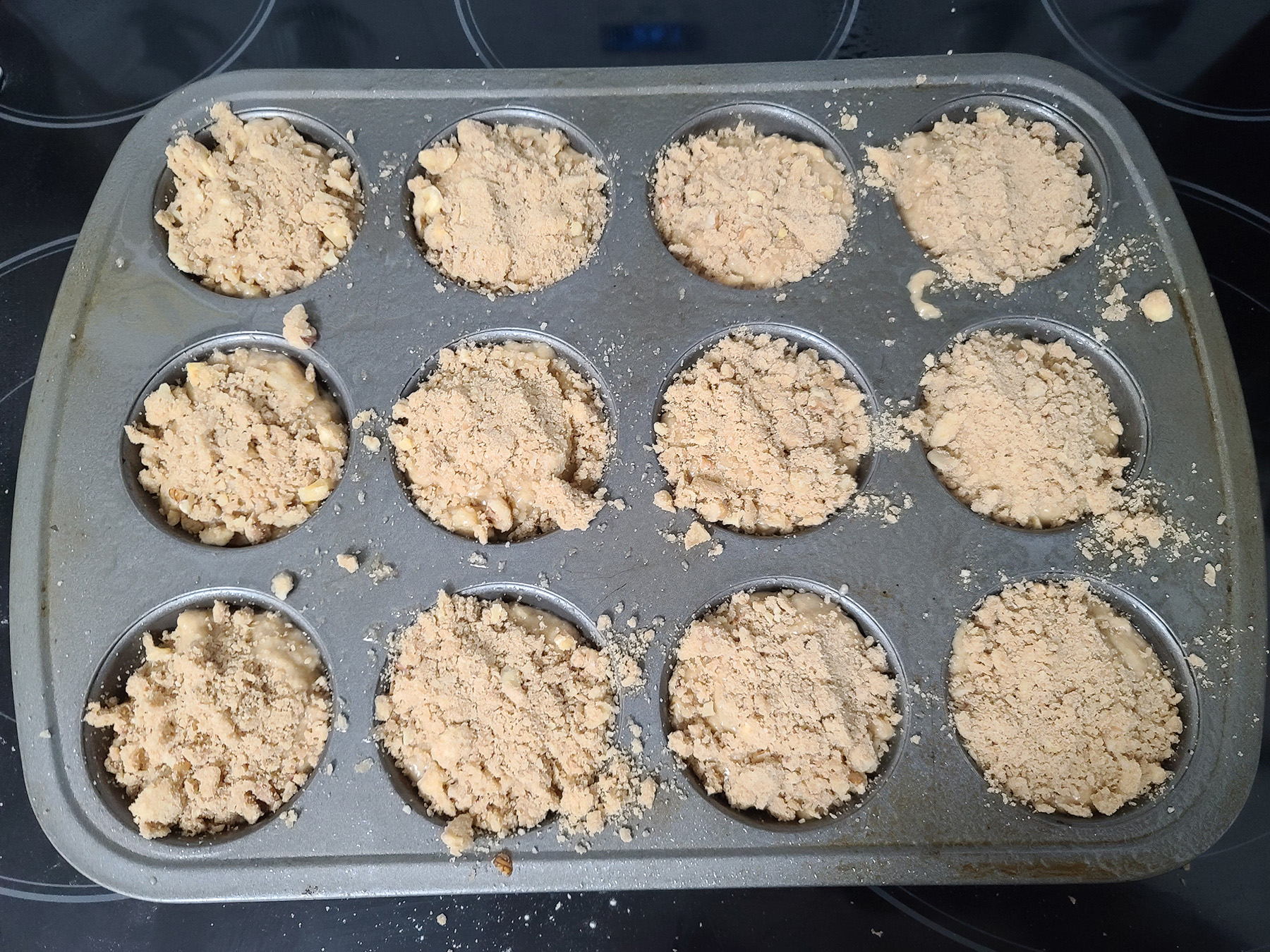 The batter in the muffin pan, with each cavity topped with streusel.