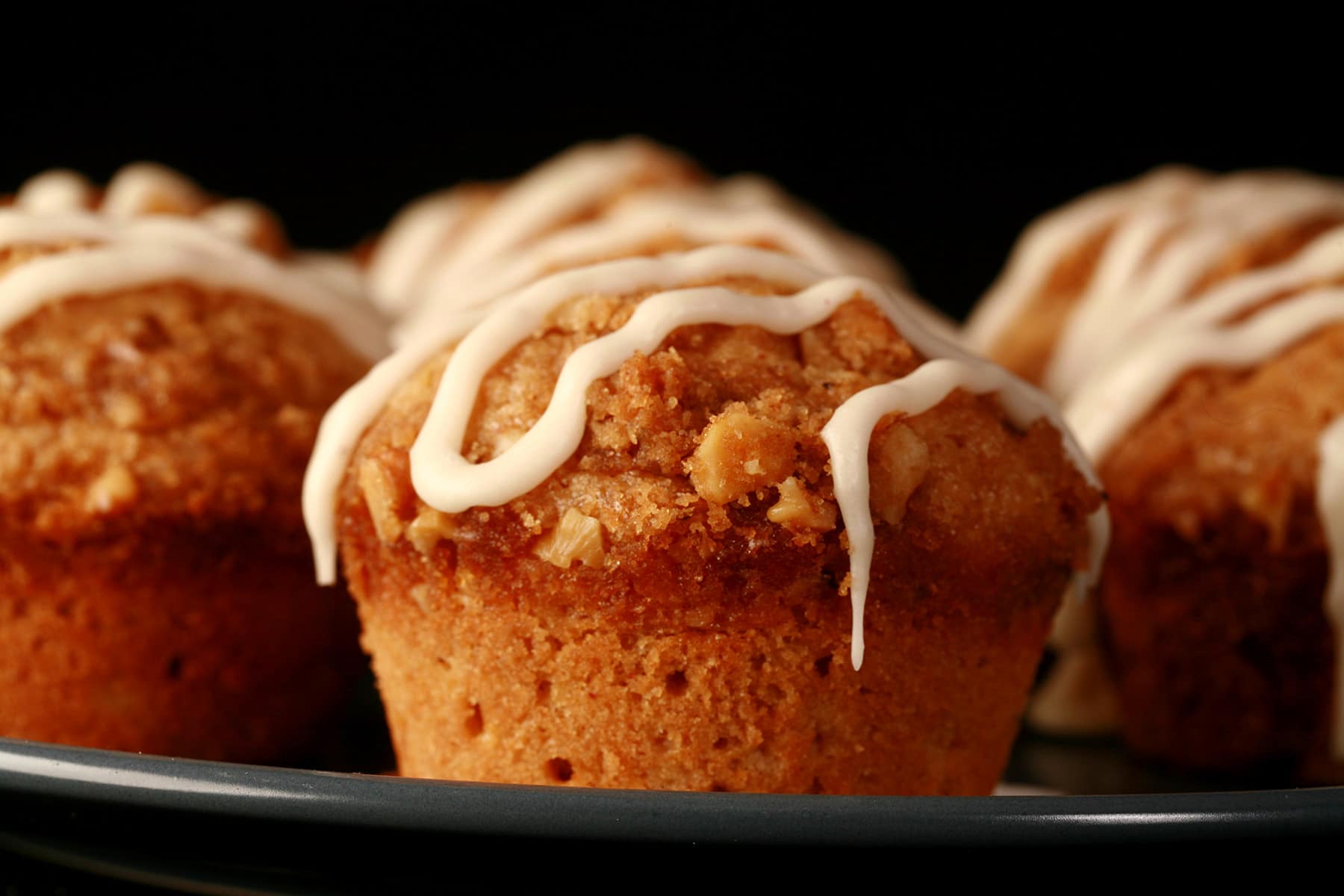 A plate of nutmeg coffee cake muffins, each drizzled with maple nutmeg glaze.