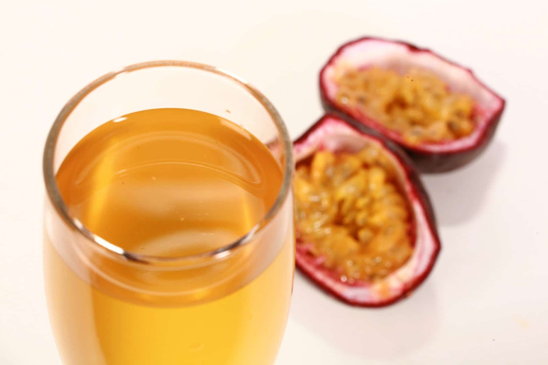 A flute of golden yellow passionfruit wine, next to a halved passionfruit.