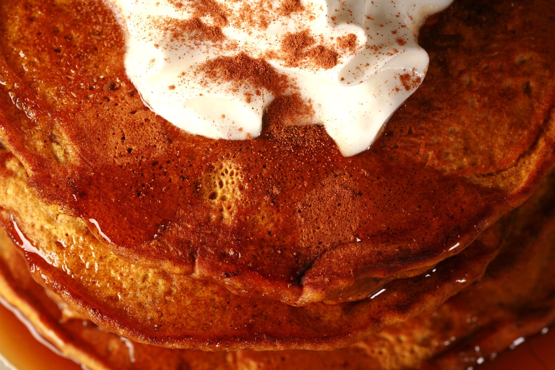 A tall stack of pumpkin pancakes, topped with whipped cream.