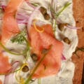 A close up view of smoked salmon pizza. The crust is rye, and it's topped with cream cheese sauce, smoked salmon, and other toppings.