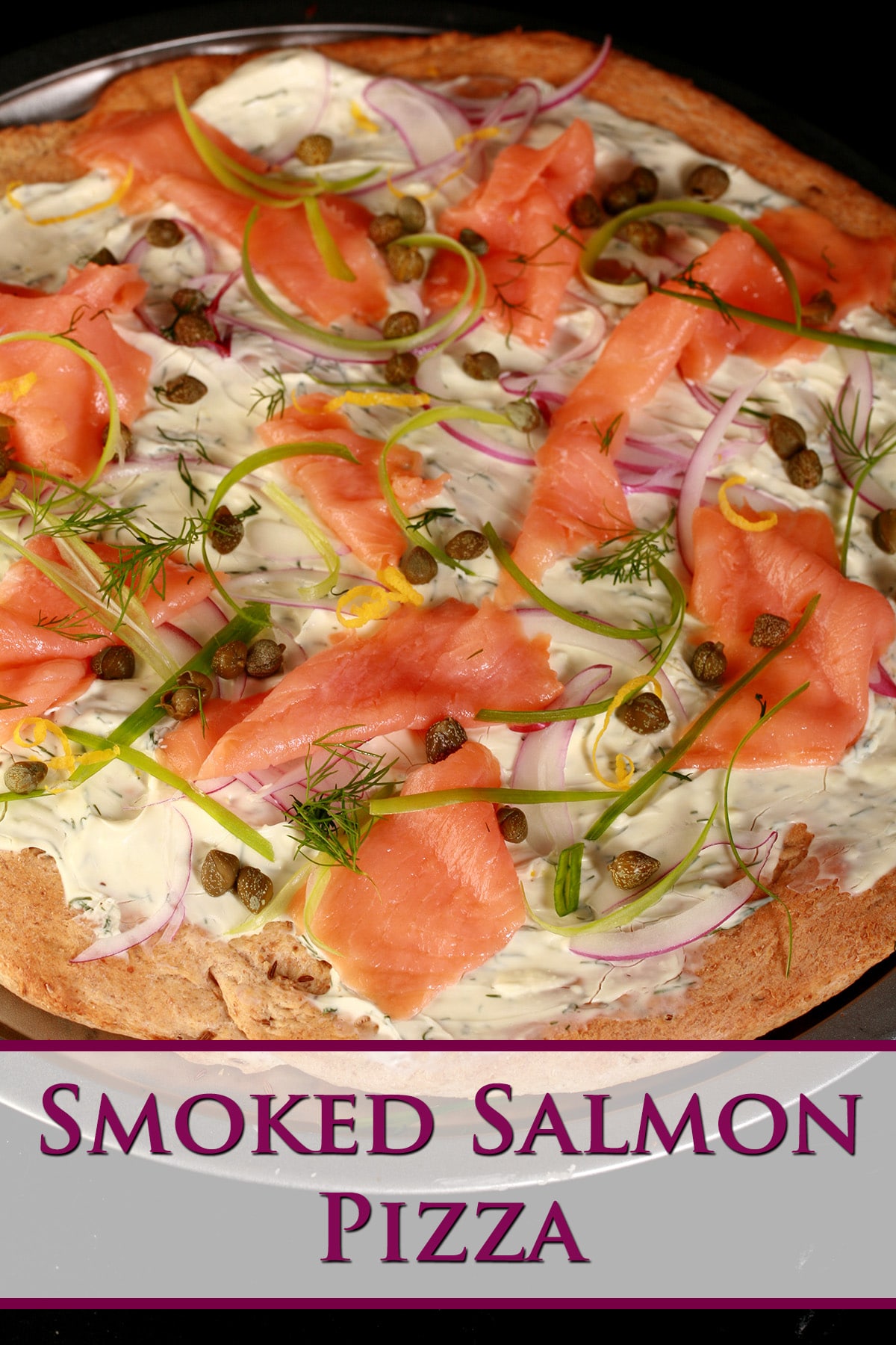 A close up view of smoked salmon pizza. The crust is rye, and it's topped with cream cheese sauce, smoked salmon, and other toppings.