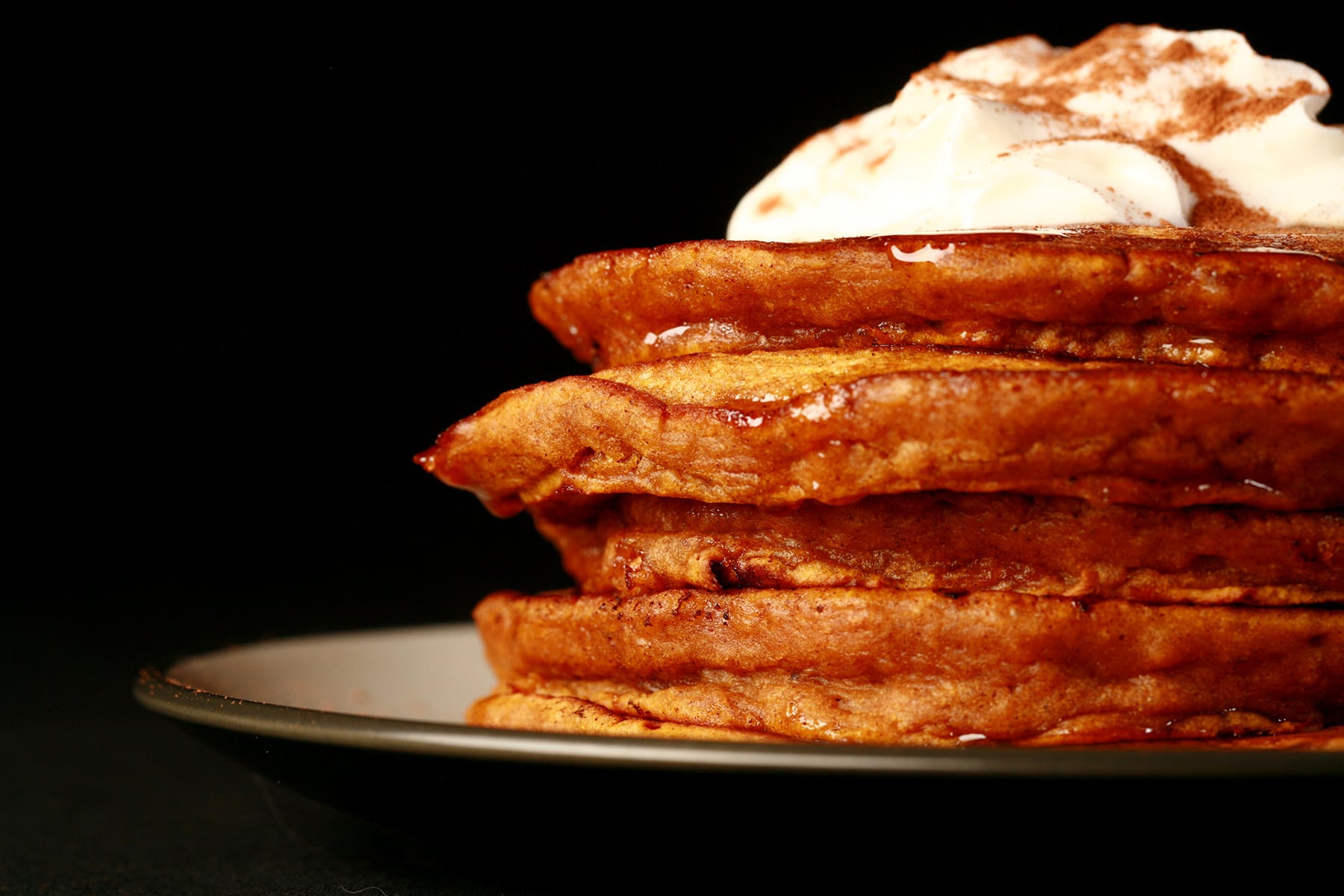 A tall stack of spiced pumpkin pancakes, topped with whipped cream.