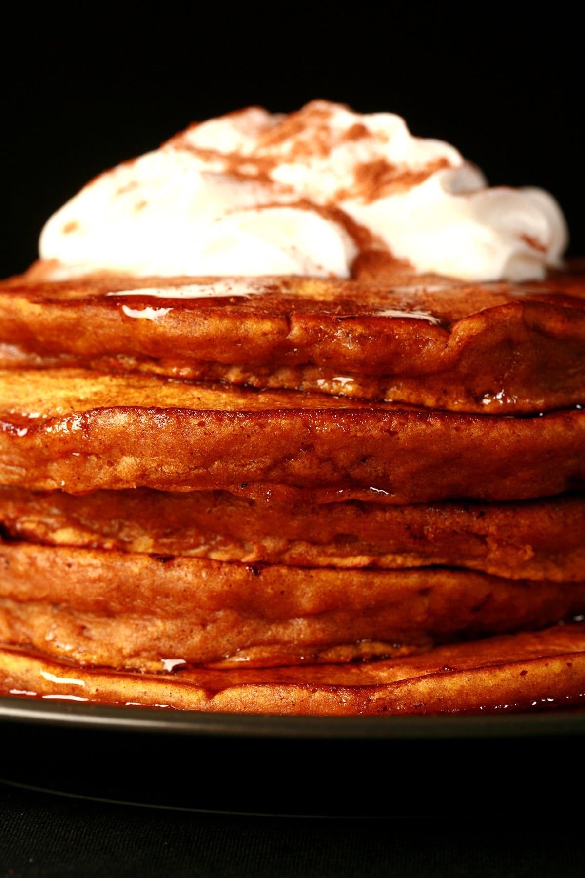 A tall stack of spiced pumpkin pancakes, topped with whipped cream.