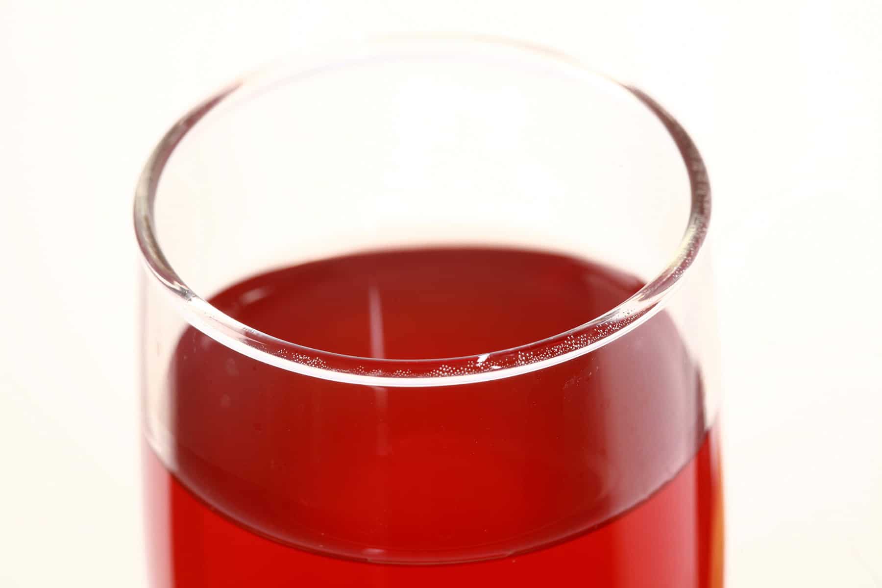 A tall glass of fruit punch-coloured stone fruit wine, next to a peach, a plum, and a few cherries.