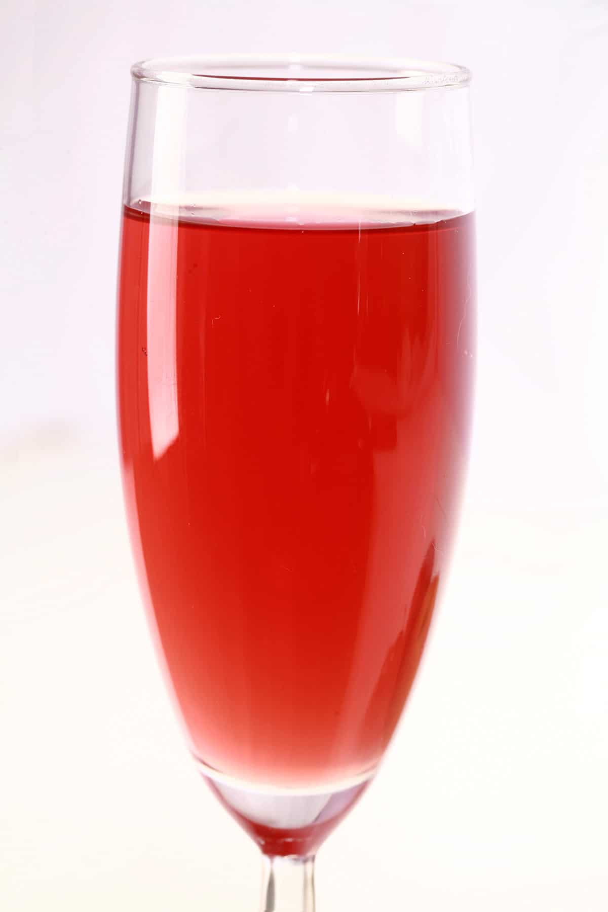 A tall glass of fruit punch-coloured stone fruit wine, next to a peach, a plum, and a few cherries.