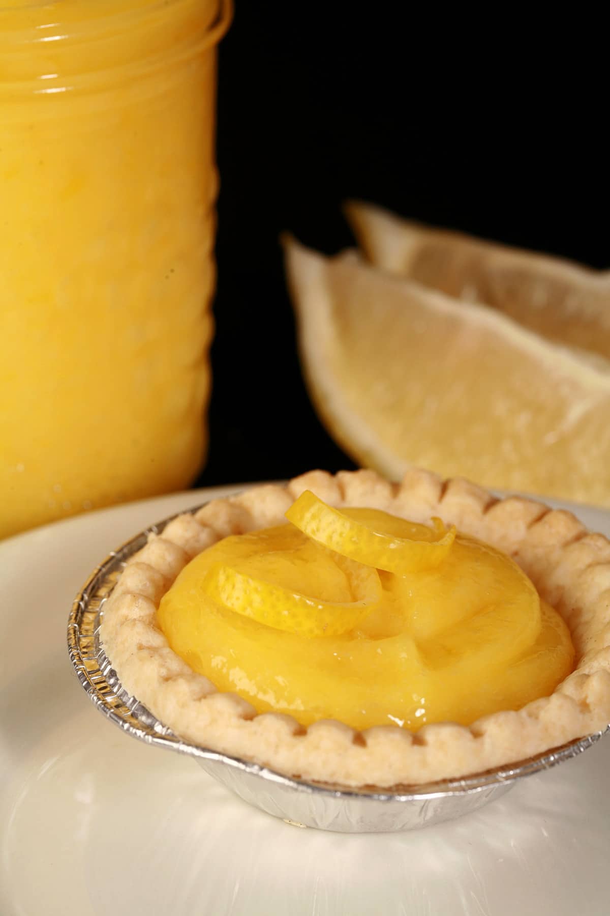 A lemon tart on a plate, next to a jar of homemade lemon curd.