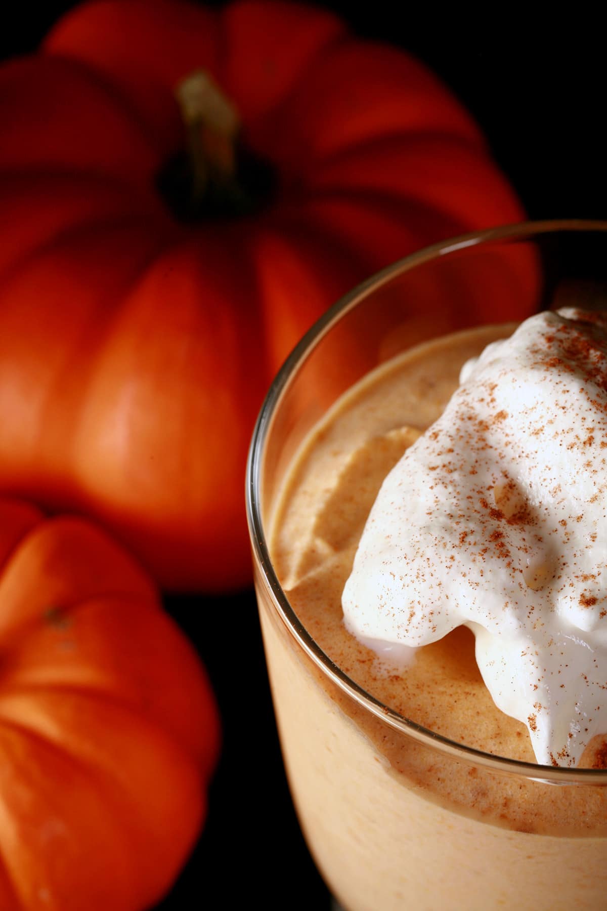 Close up photo of a glass of maple pumpkin mousse. There is whipped cream and a sprinkle of cinnamon on top.