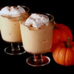 Two glasses with traditional maple pumpkin mousse in them. They are topped with whipped cream and a sprinkle of cinnamon.