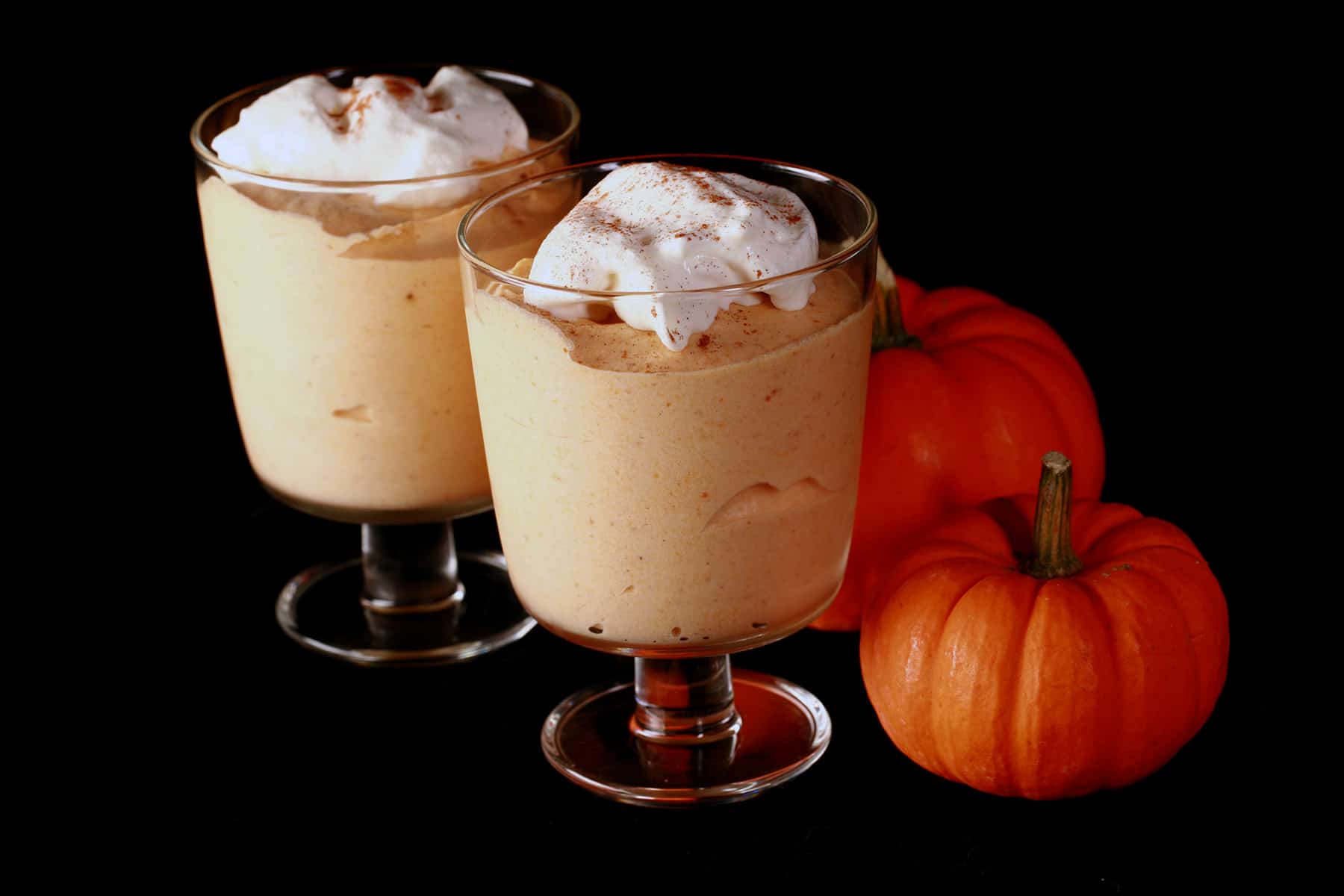 Two glasses with traditional maple pumpkin mousse in them. They are topped with whipped cream and a sprinkle of cinnamon.