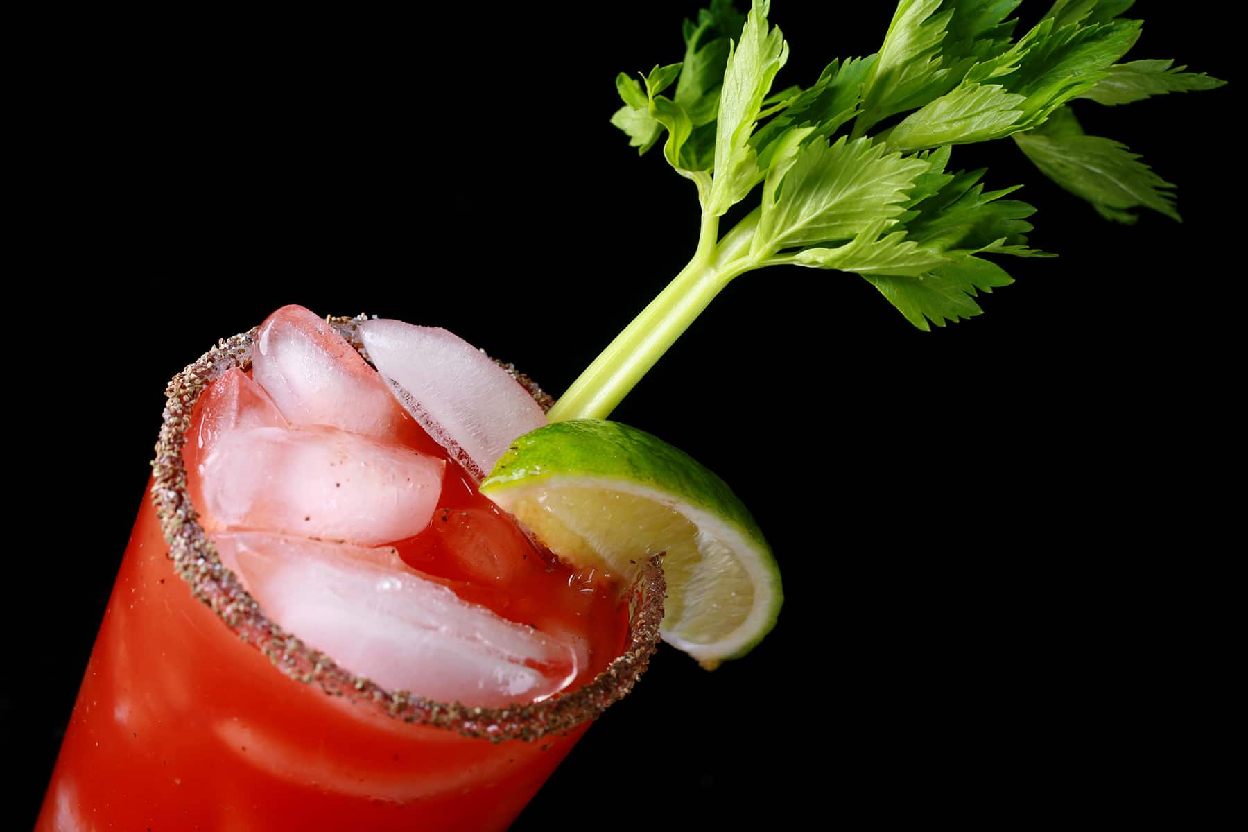 A Bloody Caesar, using homemade Clamato. A tomato based cocktail in a tall glass, with a celery stick and lime wedge as garnish.