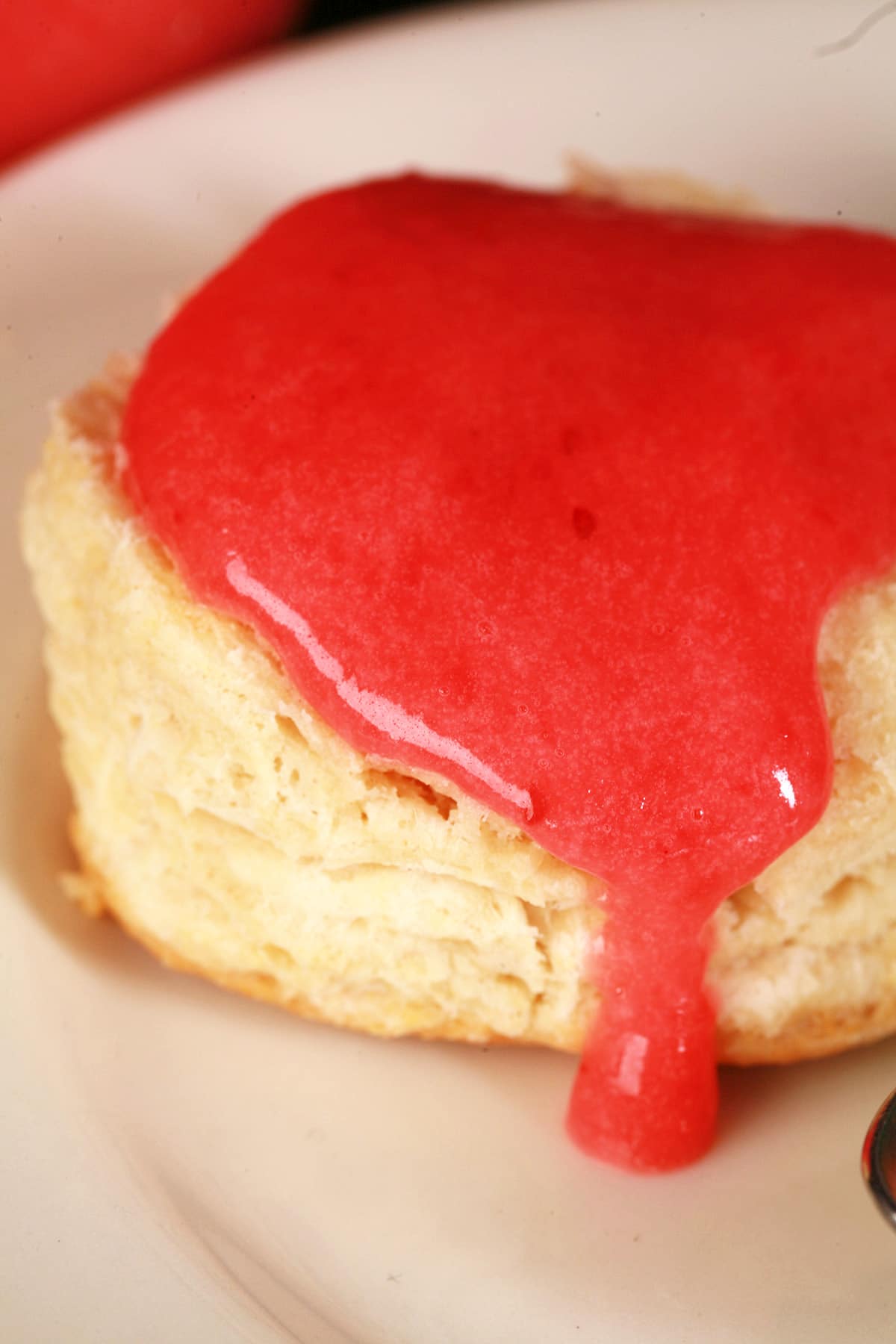 A biscuit on a white plate, with cranberry curd dripping off the biscuit.