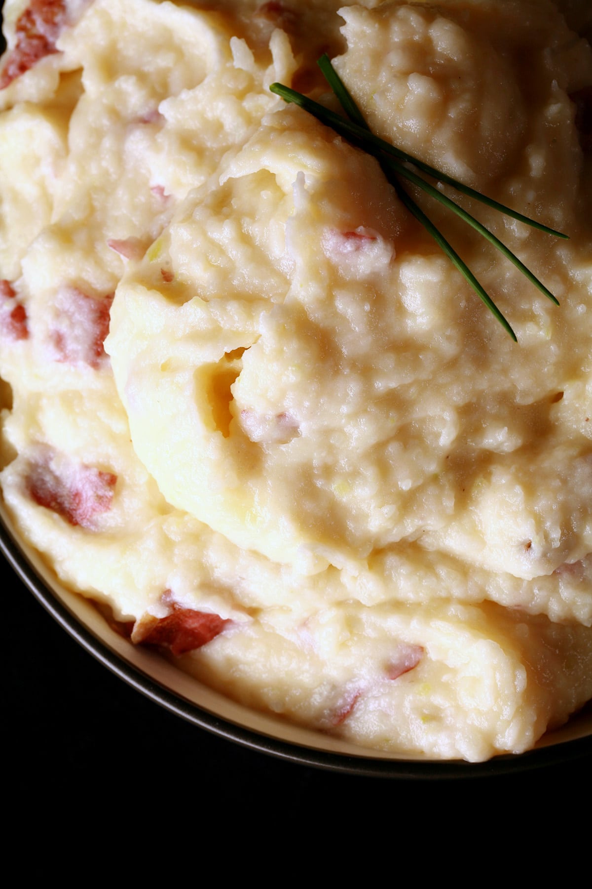 A close up photo of a bowl of gouda mashed potatoes. There are a few pieces of chives on top.