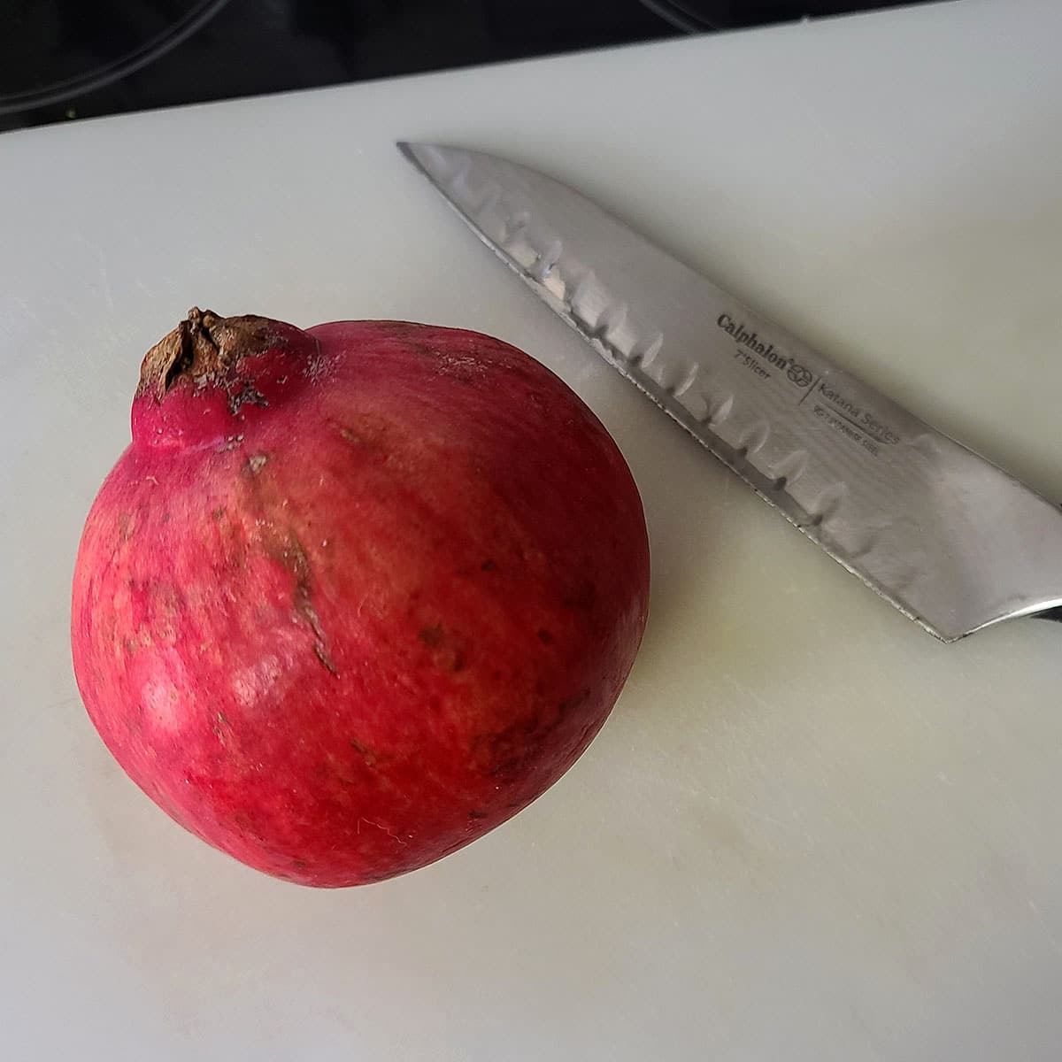 A whole pomegranate and a knife on a cutting board.