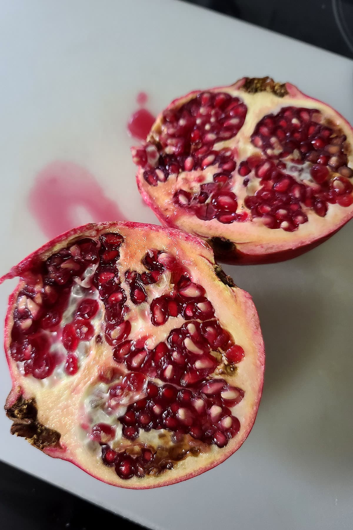 A pomegranate cut in half, on a cutting board.