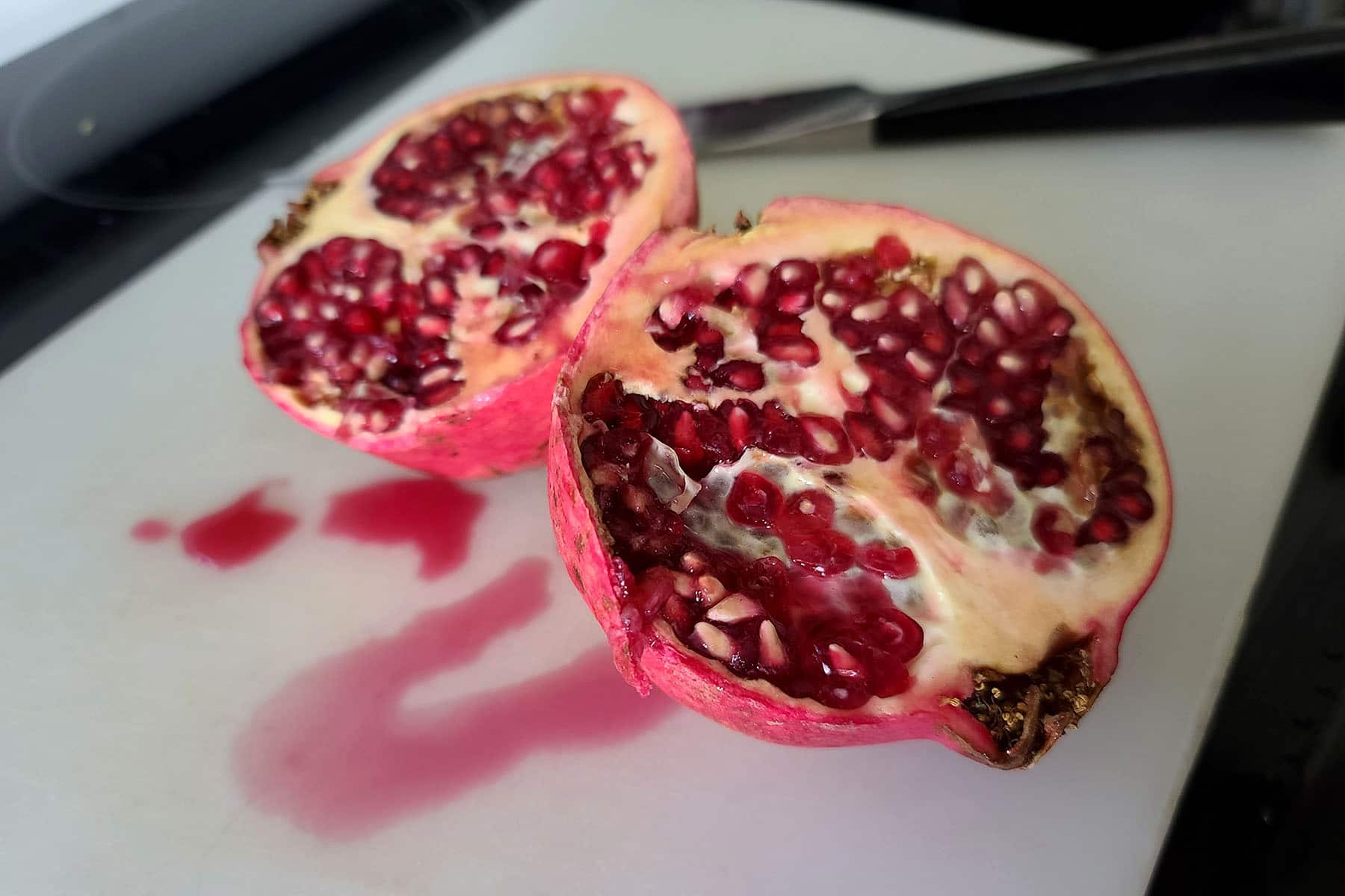 Two halves of a pomegranate on a cutting board.