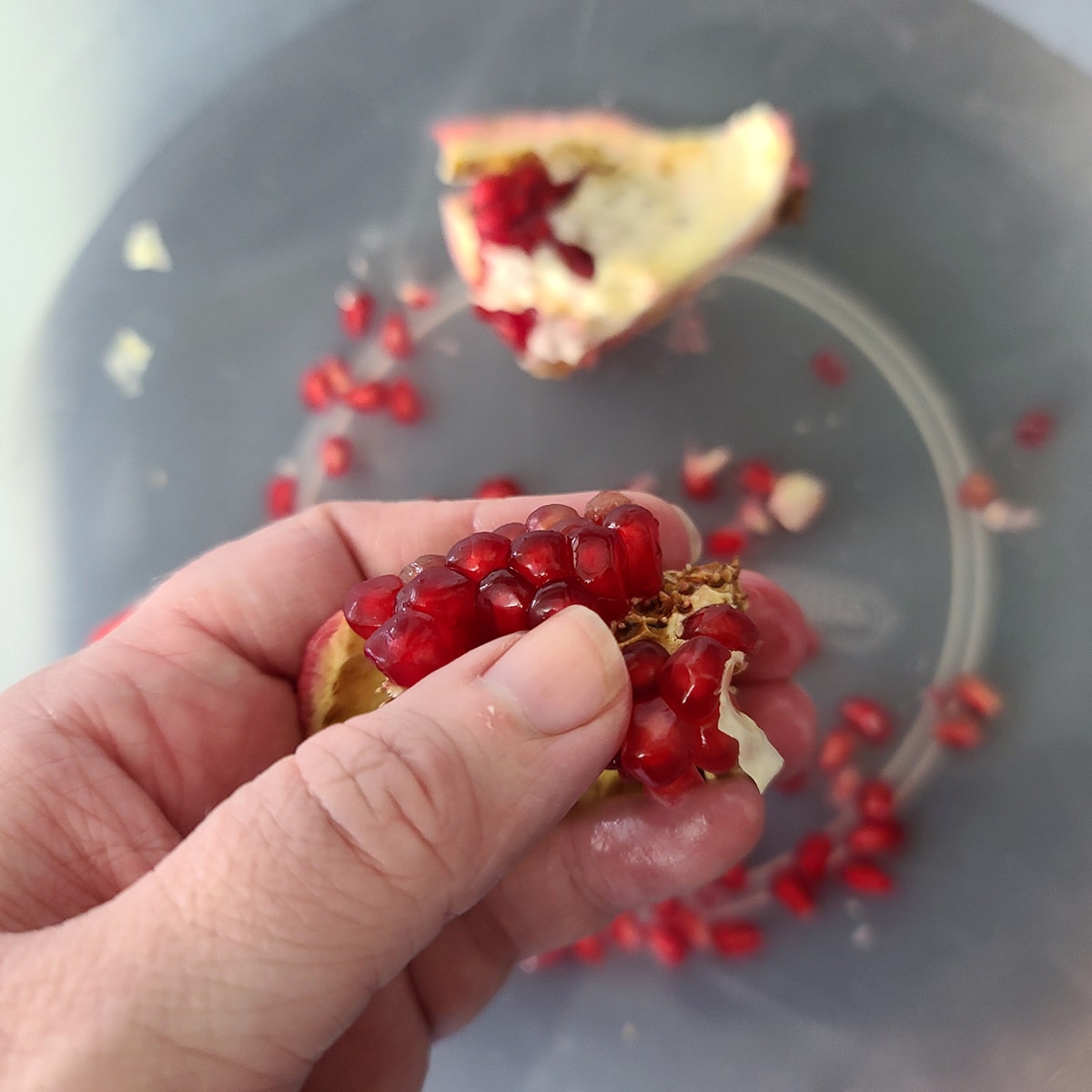 A thumb dislodging pomegranate arils from a chunk of pomegranate.