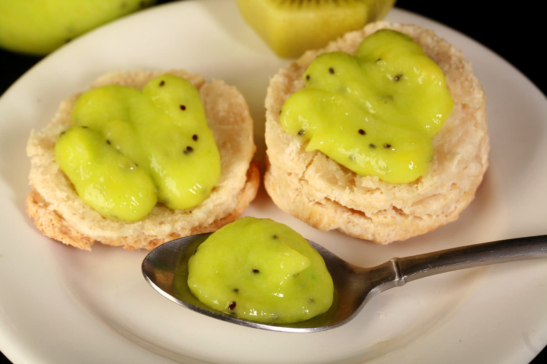 2 biscuits topped with kiwi curd, along with a spoon of curd on the same plate.