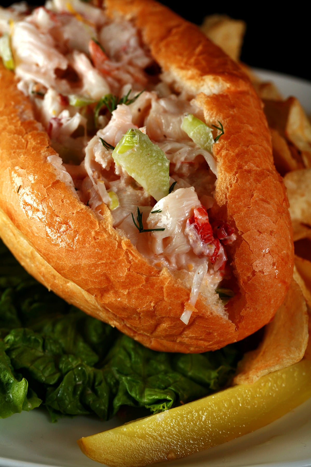 A Lobster Roll sandwich on a plate with chips and a pickle.