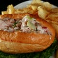 An Ultimate Lobster Roll sandwich on a plate with chips and a pickle.