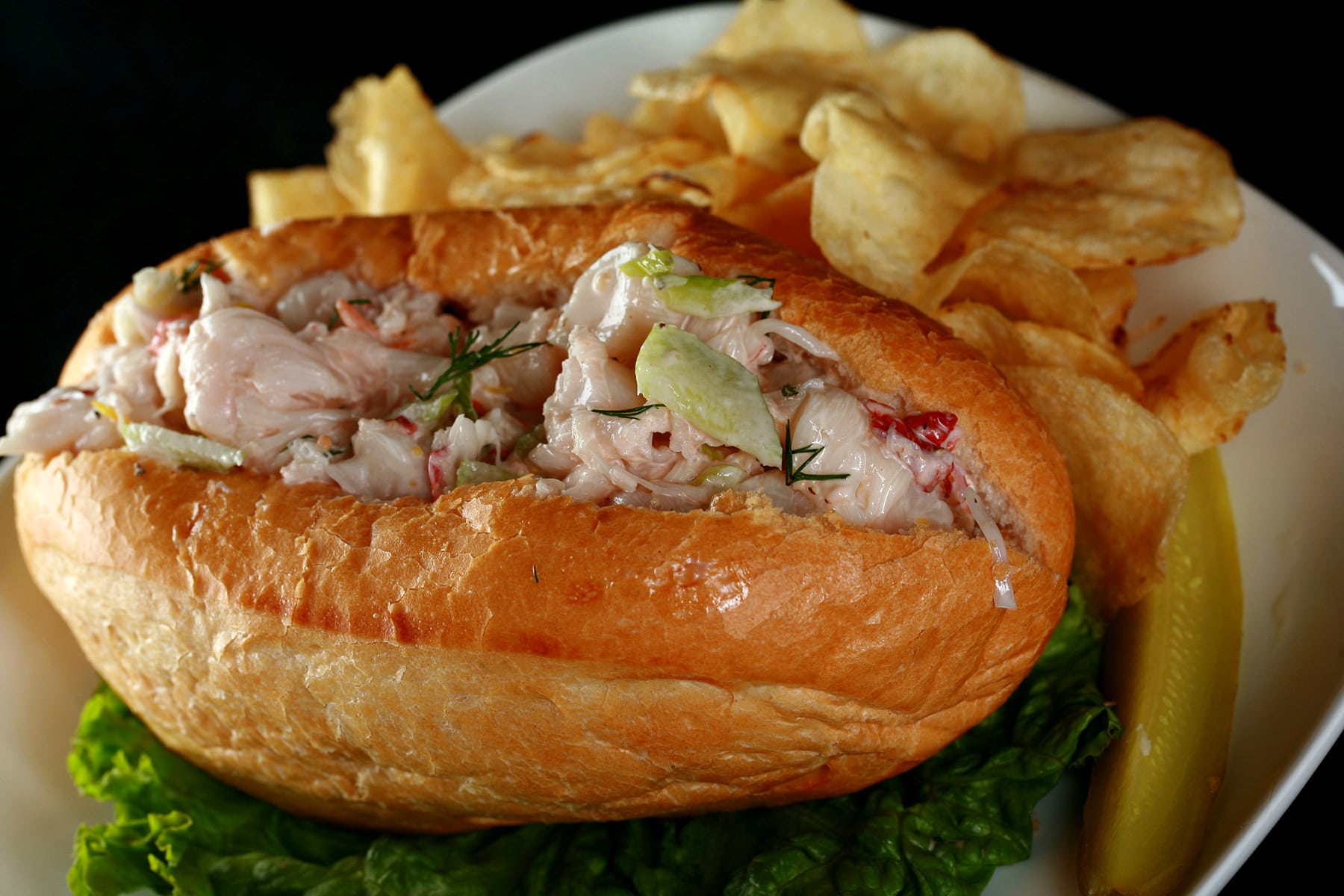 The Best Lobster Roll sandwich on a plate with chips and a pickle.