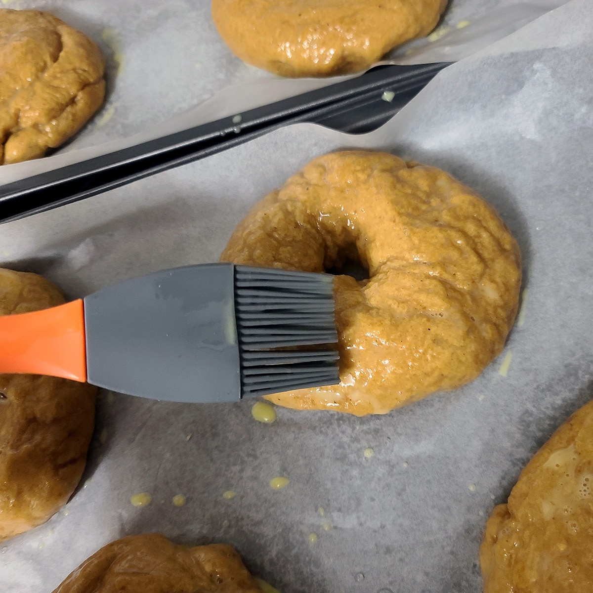 Egg wash being brushed on a pumpkin bagel before baking.