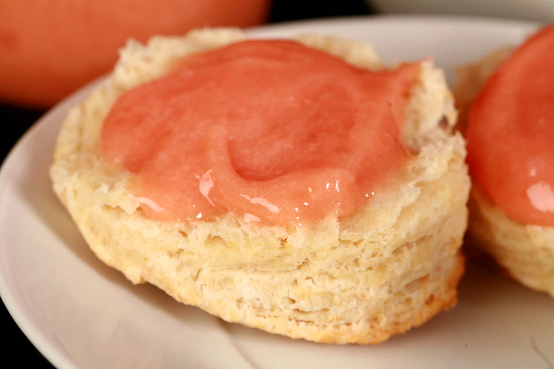 A raspberry curd covered biscuit on a plate, along with a spoon of the pink curd.