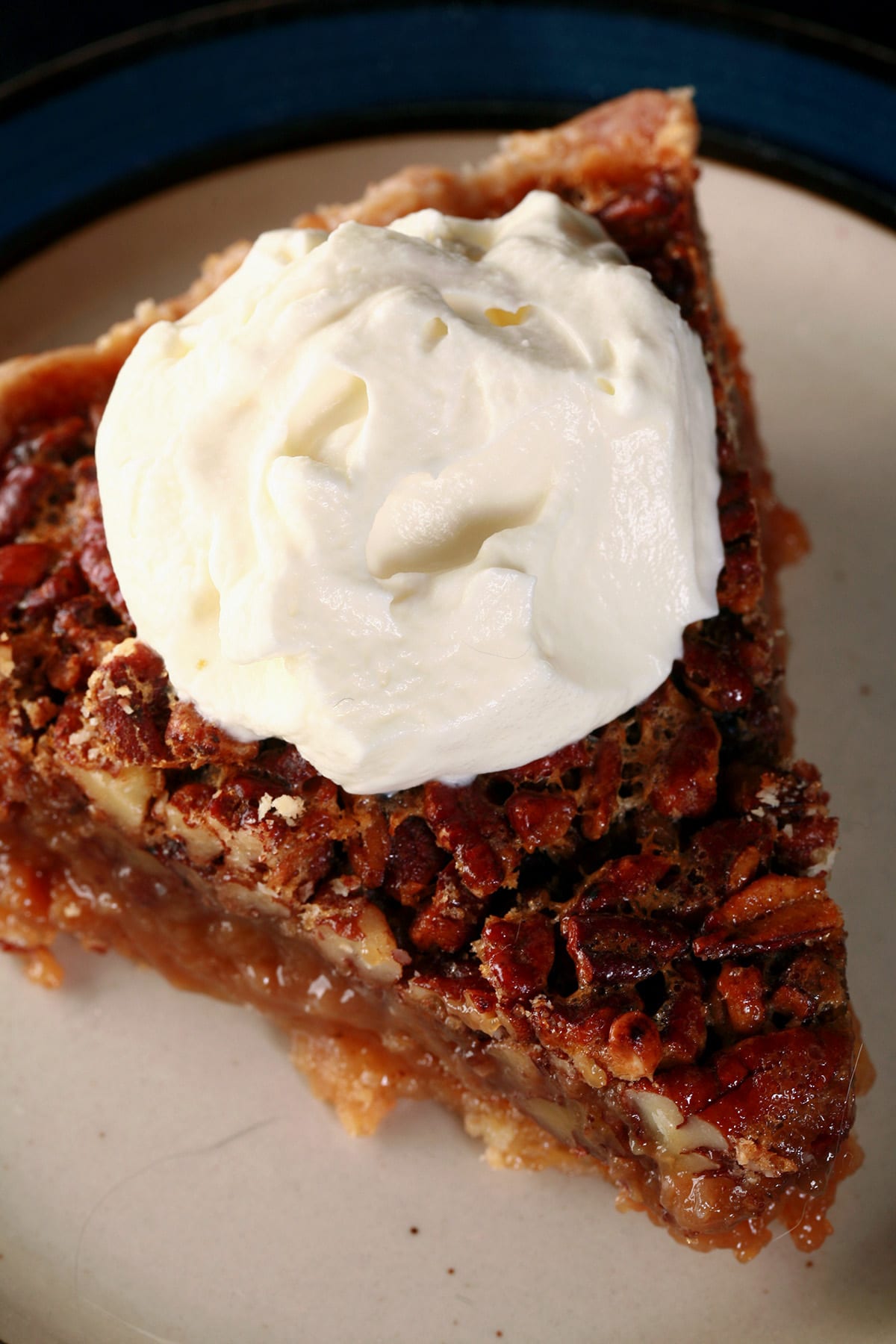 A close up view of a slice of Southern Comfort Pecan Pie, topped with boozy whipped cream.