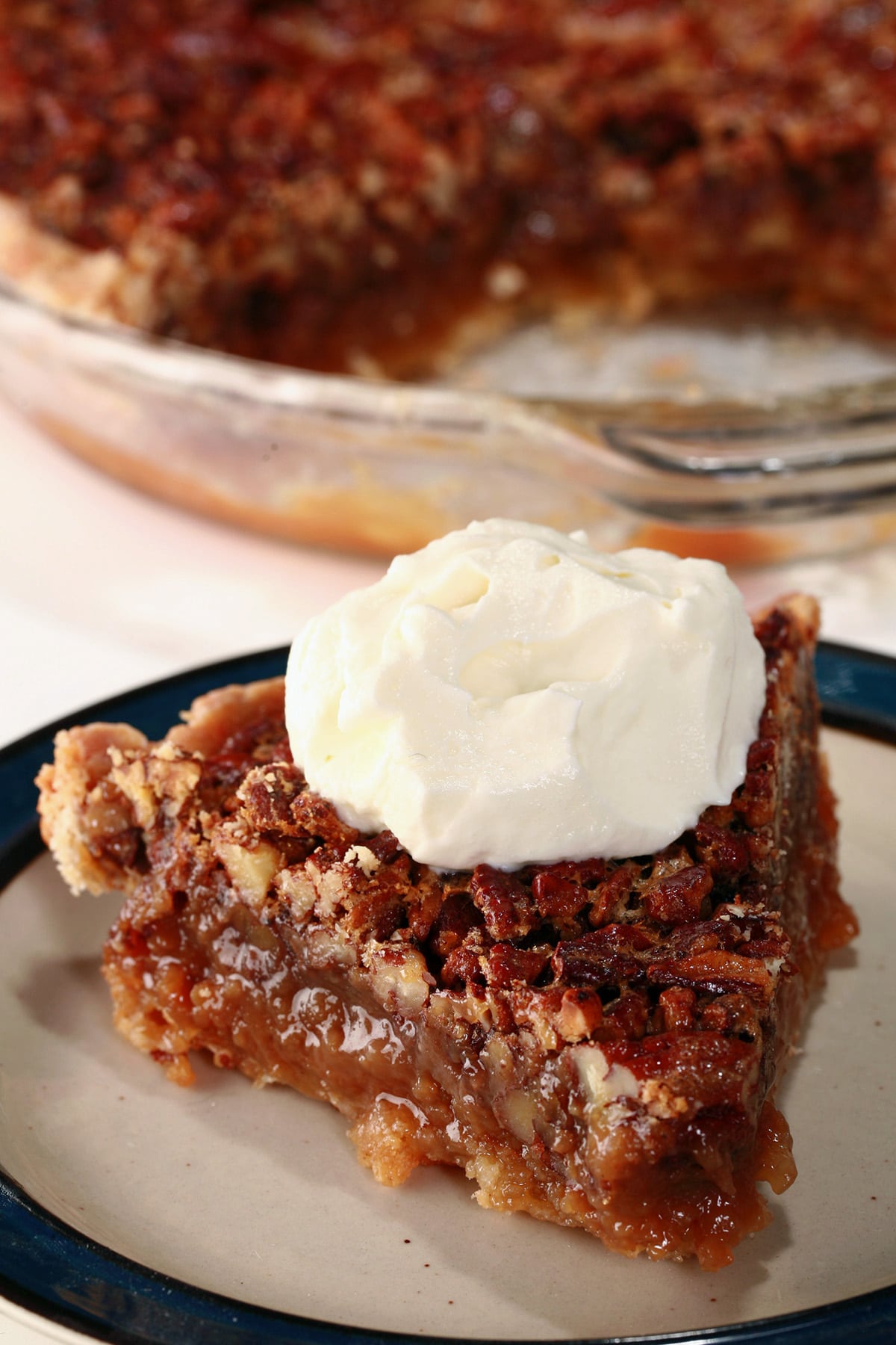 A close up view of a slice of Southern Comfort Pecan Pie, topped with boozy whipped cream.