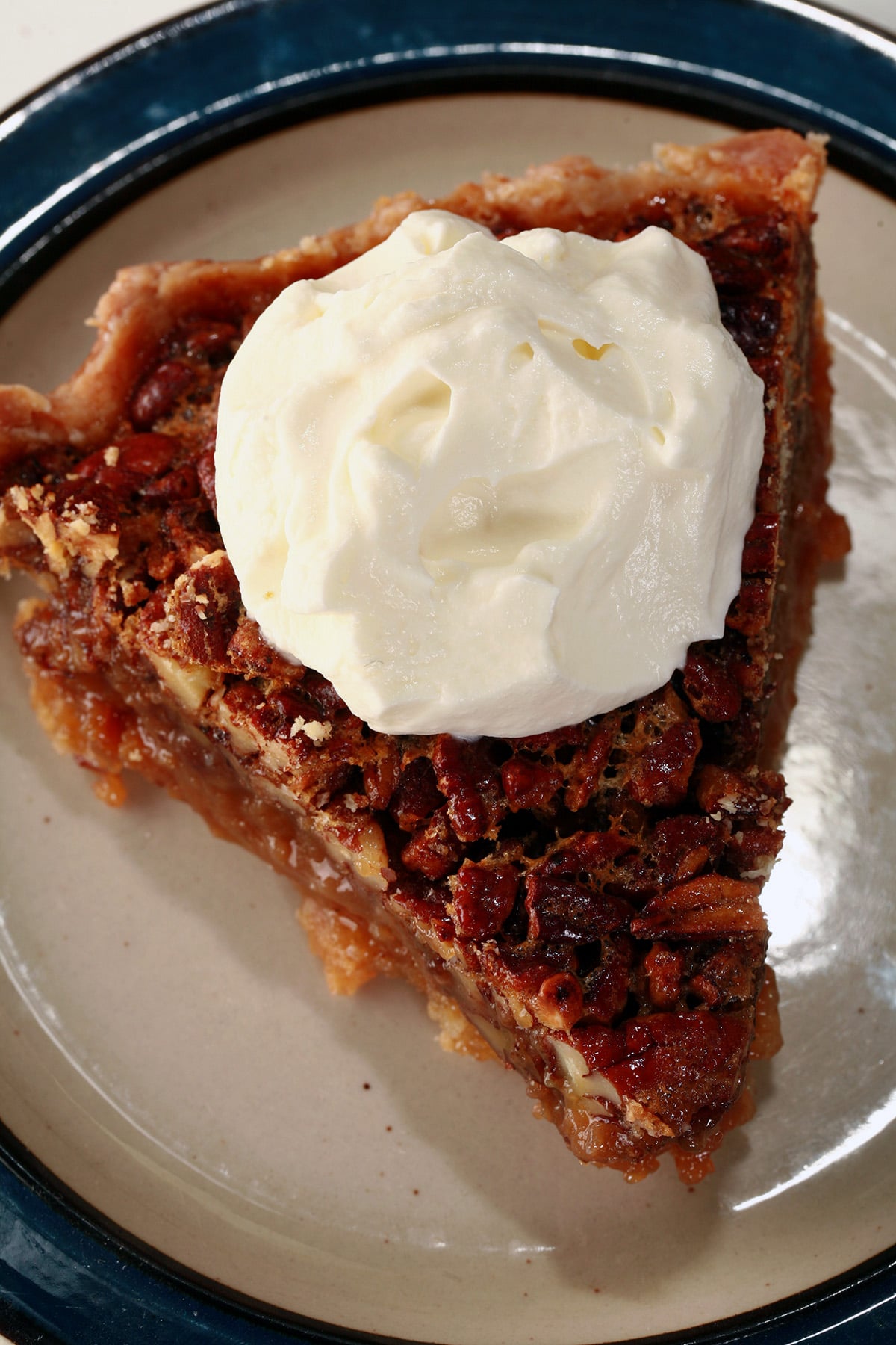 A close up view of a slice of Southern Comfort Pecan Pie, topped with boozy whipped cream.