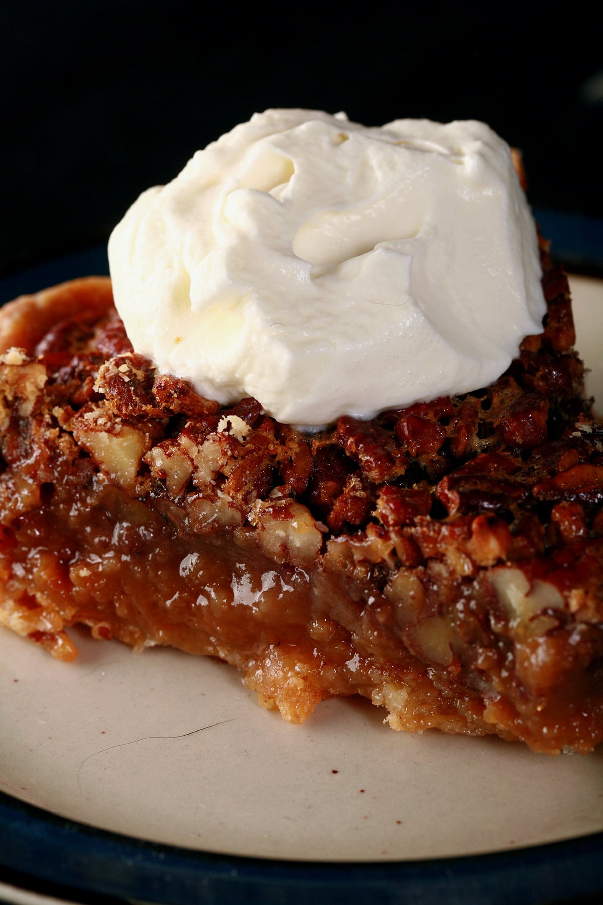 A close up view of a slice of Southern Comfort Pecan Pie, topped with boozy whipped cream.